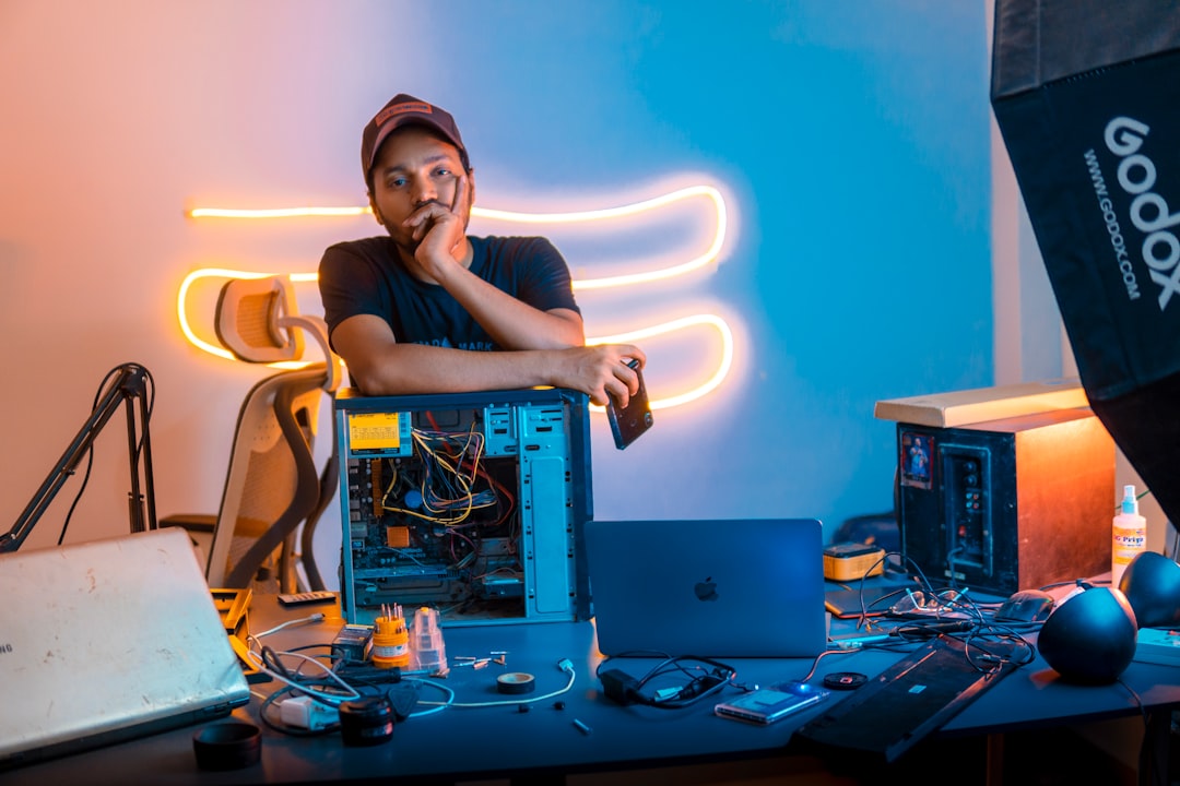 A tech enthusiast leans on an open CPU, surrounded by gadgets and tools on a vibrant, neon-lit workspace, reflecting a creative and tech-savvy vibe.